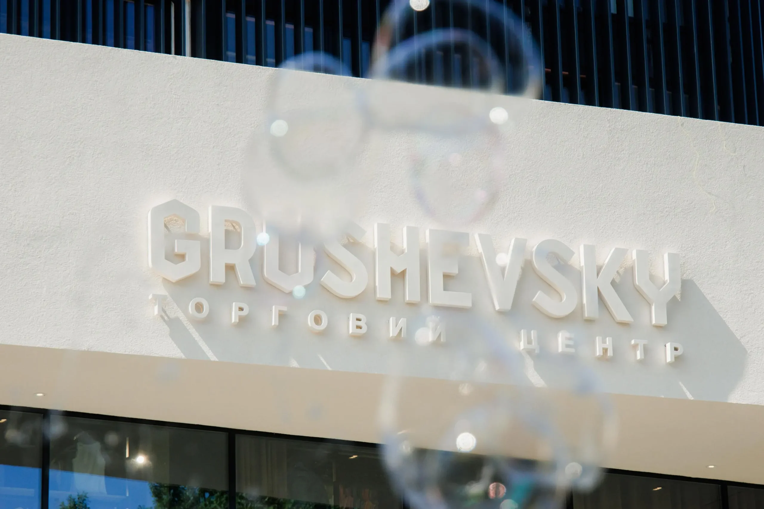 Вивіска "Grushevsky торговий центр" великим планом на фасаді будівлі крізь мильні бульбашки.